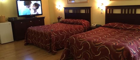 A hotel room with two beds, a television, a small refrigerator, and a nightstand with a lamp.