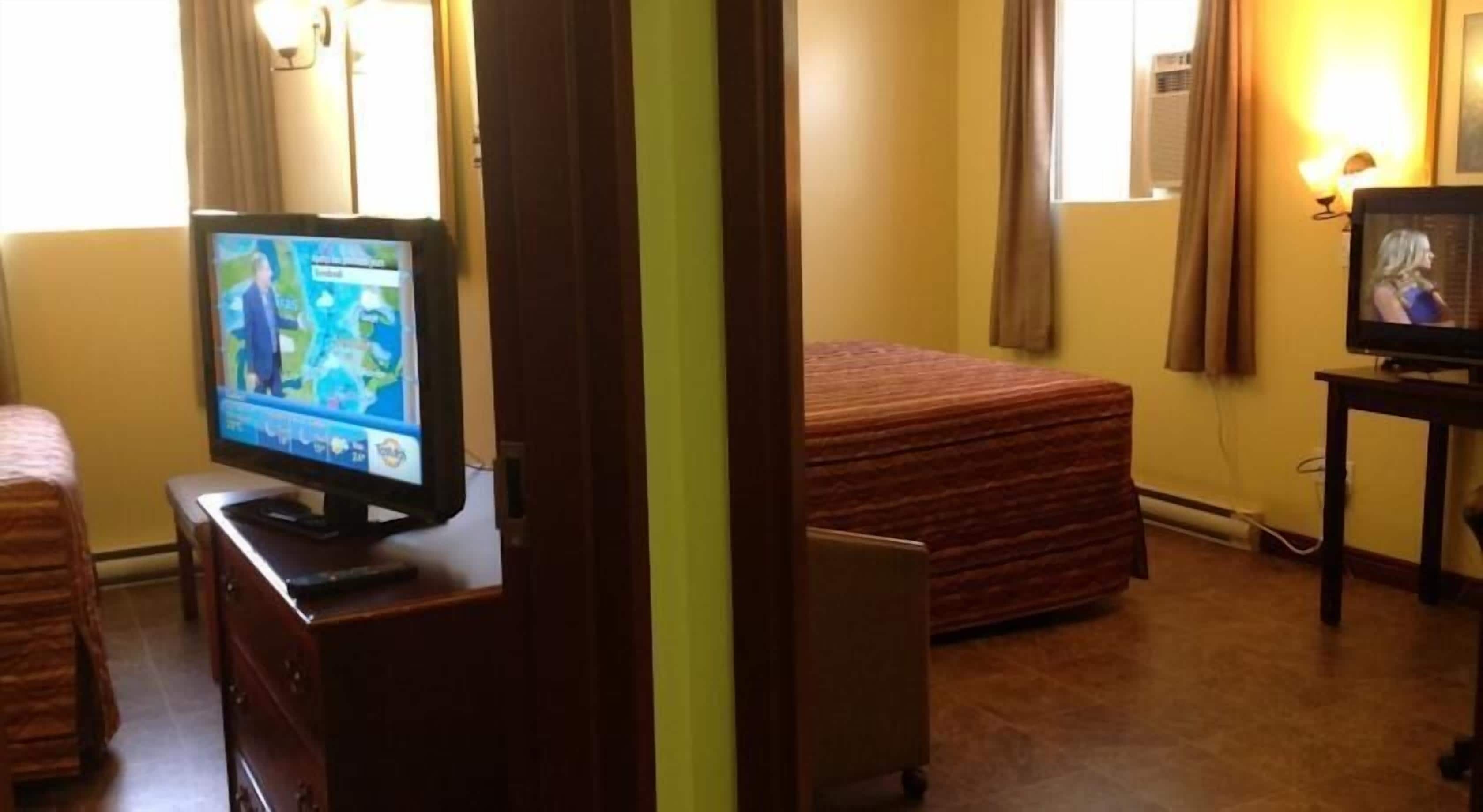 A hotel room with a television on a dresser, a bed with a striped bedspread, and a small table with a lamp.