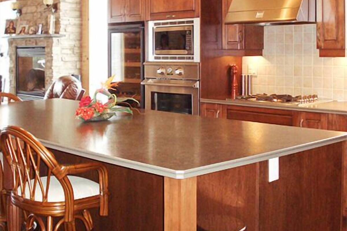 A kitchen with wooden cabinets, a large island, a stone wall, and hanging lights.