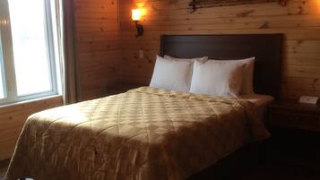 A wooden-paneled room with a bed, a nightstand, a painting, and a window.