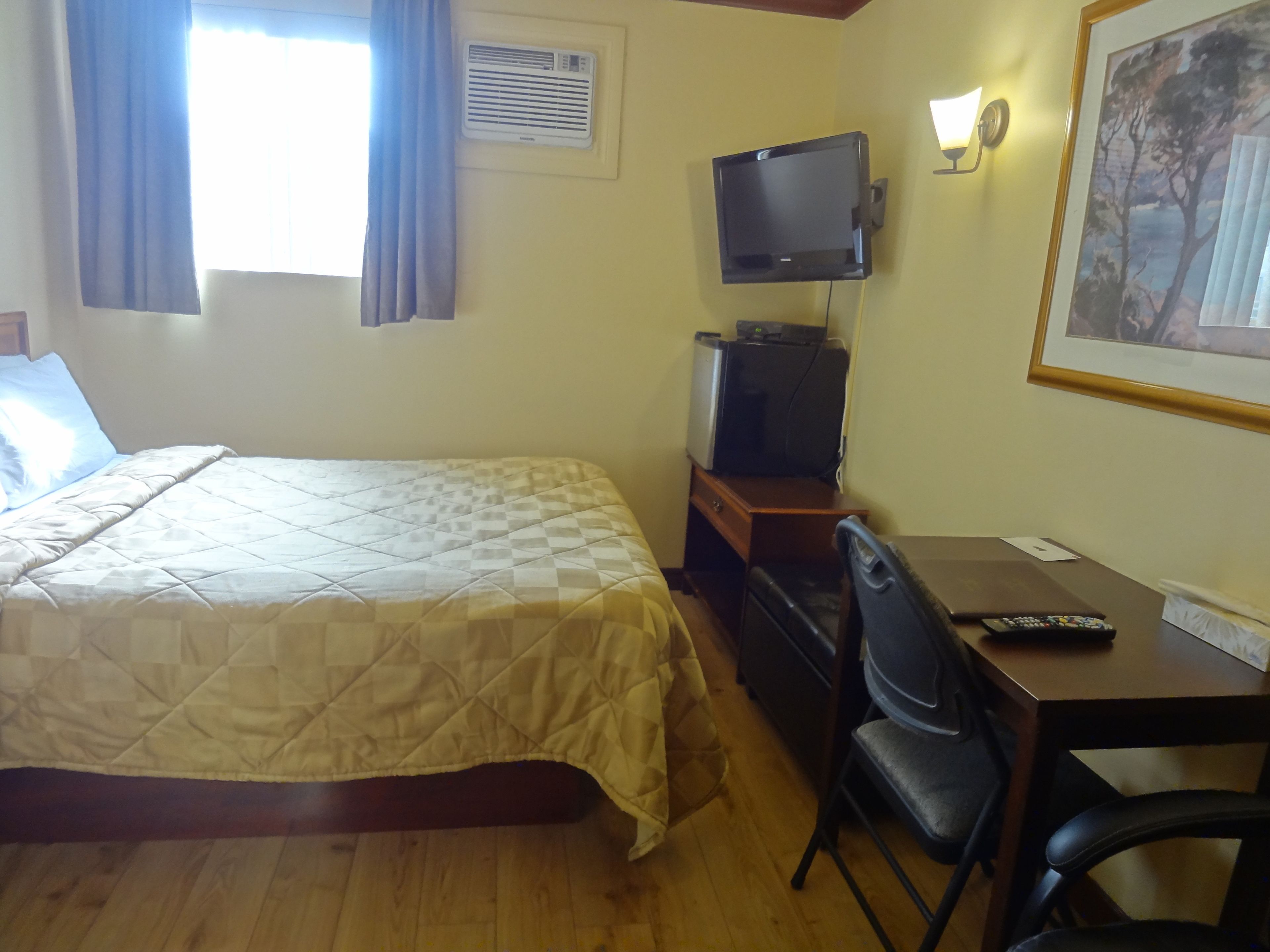A hotel room with a bed, a desk with a chair, a television, and a framed picture on the wall.