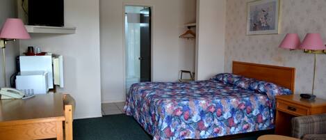 Una habitación de hotel con cama, escritorio, silla, televisión, lámpara y puerta.