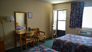 A hotel room with two beds, a desk with a telephone, a chair, a mirror, and a door leading to the outside.
