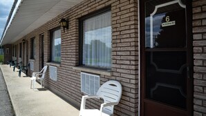 A motel with a brick facade, numbered room 6, and outdoor seating with plastic chairs.