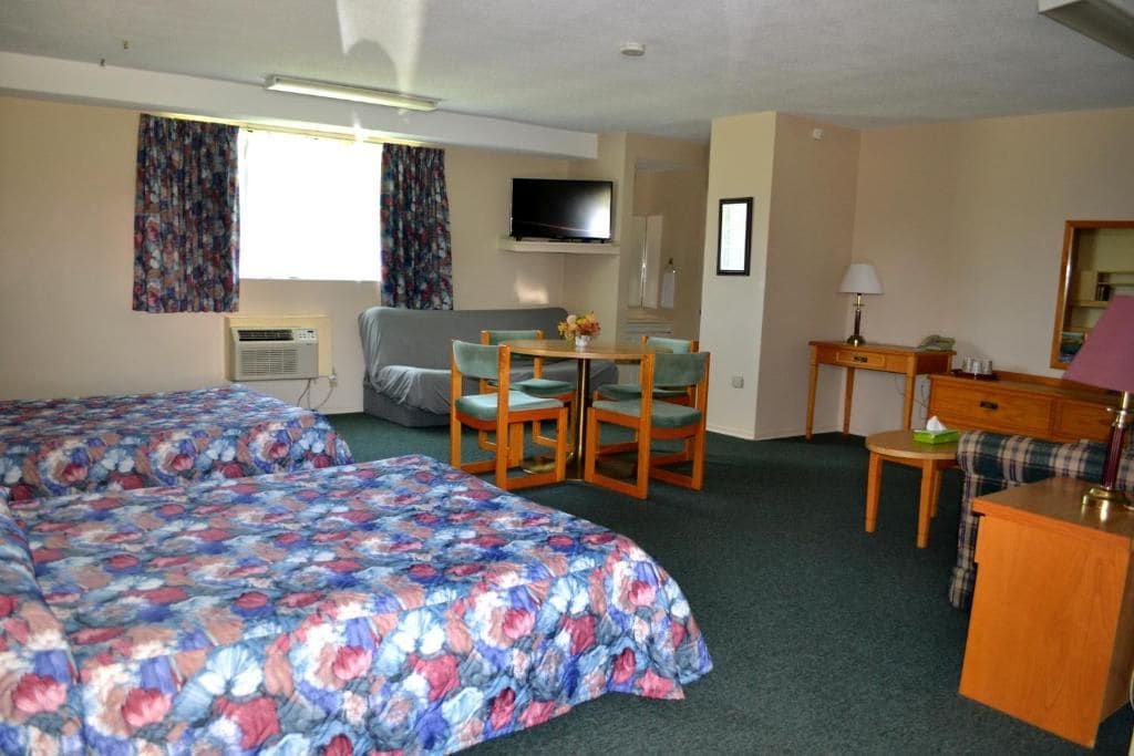 Habitación de hotel con dos camas, televisión, escritorio con lámpara y una silla.