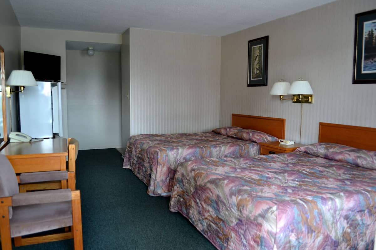 Una habitación de hotel con dos camas, un escritorio, una silla y un televisor.