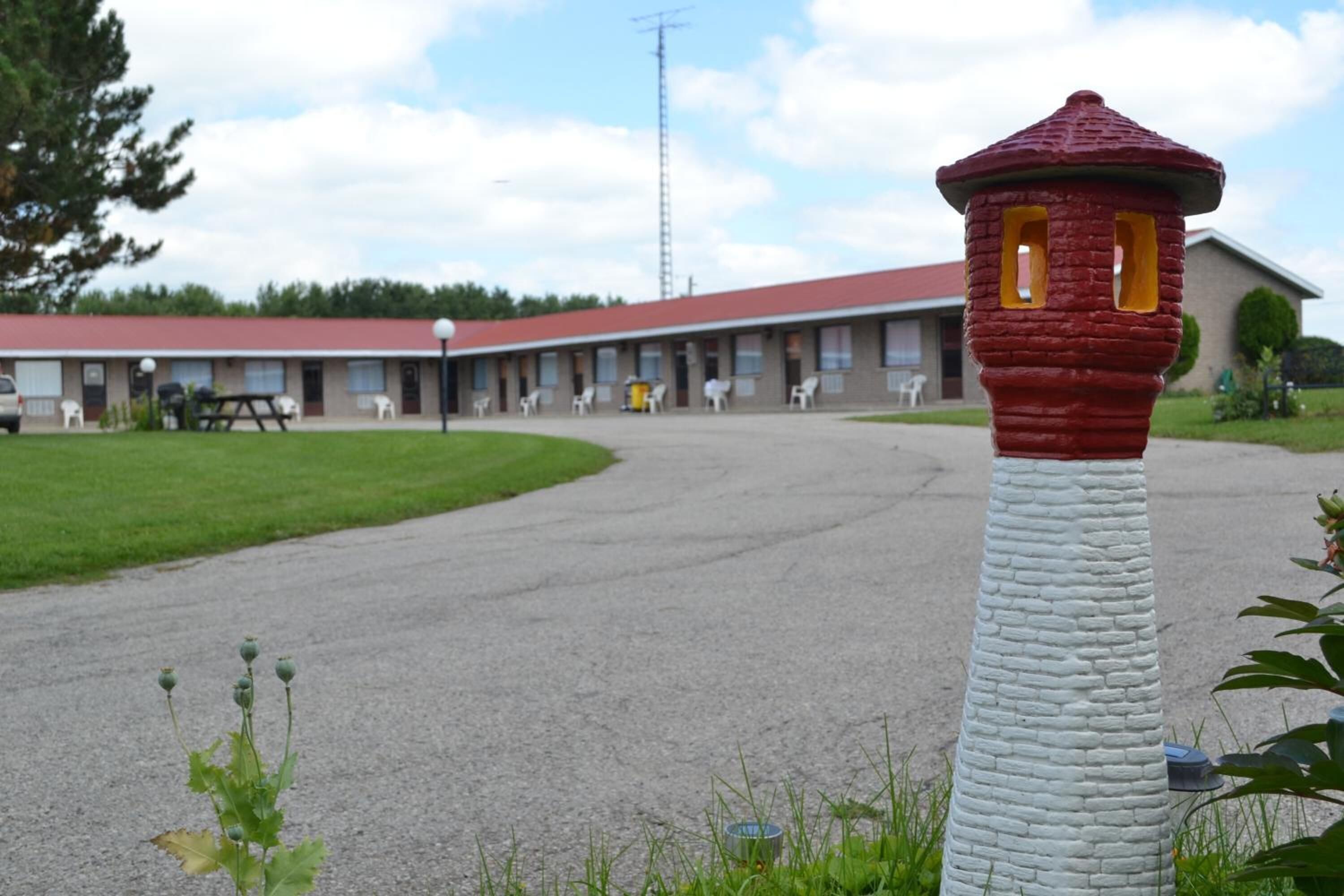 Ein Motel mit einer Reihe von Zimmern, einer zentralen Grünfläche und einer roten und weißen, turmartigen Struktur im Vordergrund.