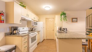 Una cocina compacta equipada con microondas, estufa y refrigerador. Incluye un cubo de basura y un lavamanos pequeño.