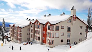 A multi-story hotel with a snow-covered roof and a ski slope in front.
