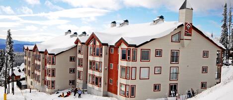 Un hotel de varios pisos con tejado nevado y una pista de esquí delante.