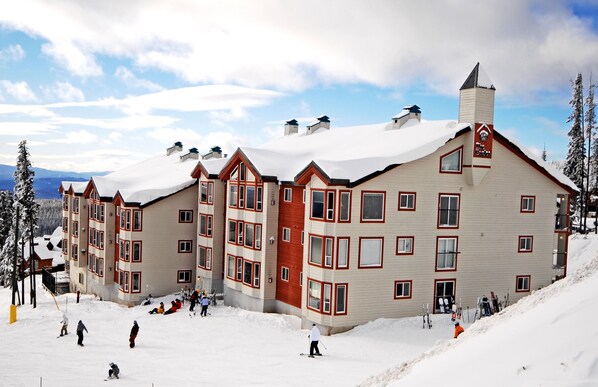 A multi-story hotel with a snow-covered roof and a ski slope in front.