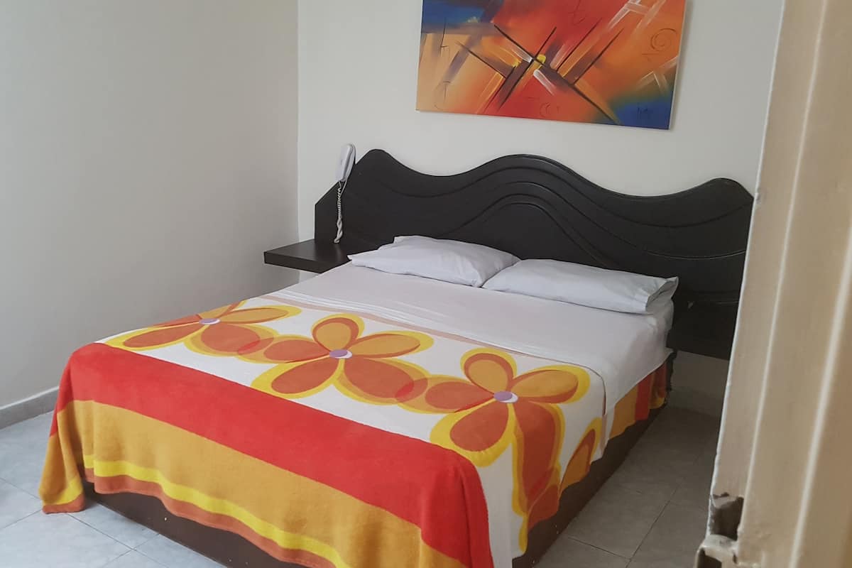 A bed with a floral bedspread, a bedside table with a lamp, and a chair.