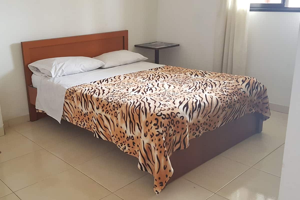 A bed with a leopard print bedspread, a wooden headboard, and a small bedside table with a tray.