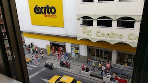 A busy street scene with a yellow taxi, pedestrians, and a building with a sign reading "éxito vecino". - Hotel Vermon (Armenia)