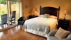 Un dormitorio con una cama grande, dos mesitas de noche con lámparas, una silla y vistas a un patio exterior a través de un ventanal corredero.