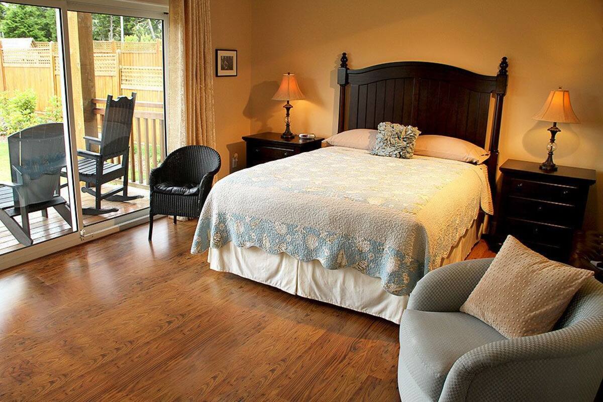 A bedroom with a large bed, two bedside tables with lamps, a chair, and a view through a sliding glass door to an outdoor patio area.