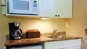 Una cocina compacta con armarios blancos, microondas, cafetera y refrigerador.