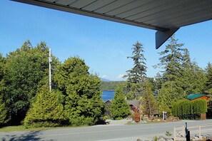 A view of a road with a bridge overhead, surrounded by dense green trees and a body of water in the background. - Ocean Mist Guesthouse (Ucluelet)