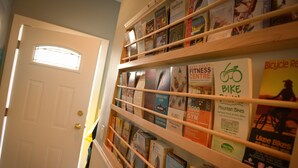 Un pasillo con una estantería que contiene varios libros y folletos, incluyendo títulos como "West Coast Fitness Centre" y "Bicycle Repair".