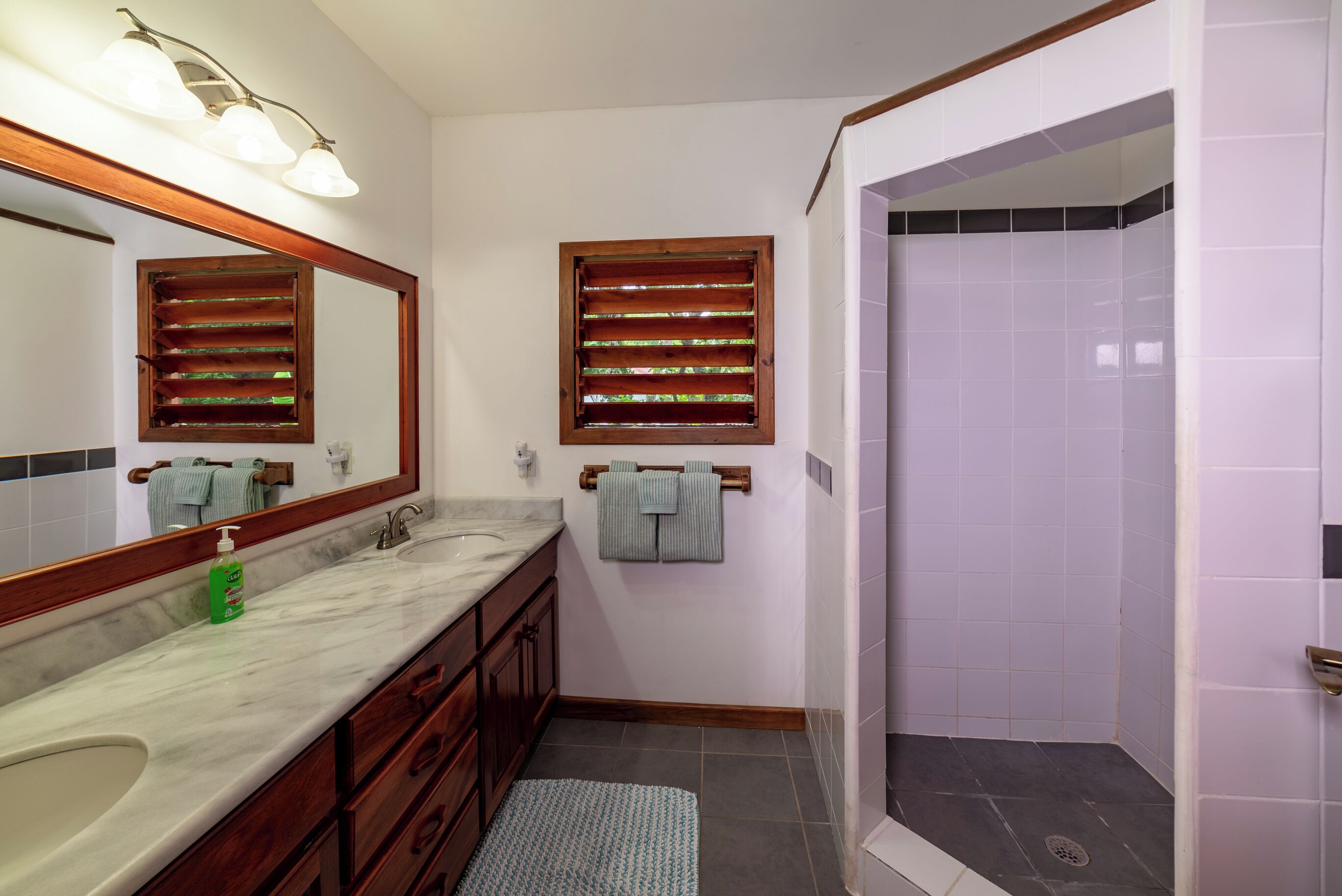 A bathroom with two sinks, a large mirror, wooden window blinds, and a shower area.