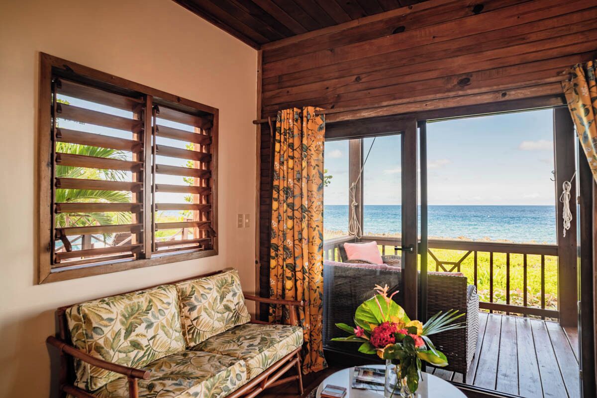 Une terrasse en bois avec un canapé et des fauteuils en osier, donnant sur une plage.