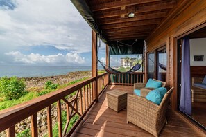 A wooden deck with wicker furniture and a hammock overlooking a rocky coastline.