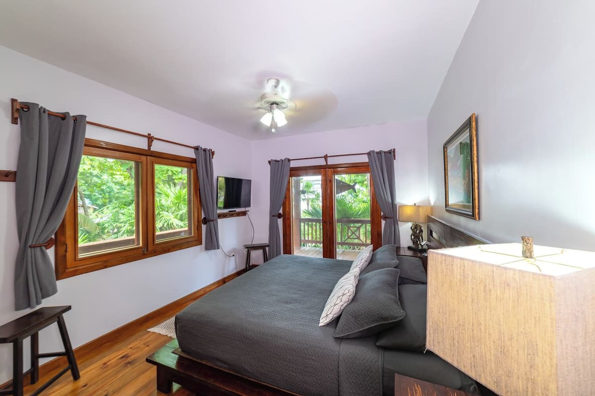 Un dormitorio con cama, televisor, ventilador de techo y ventana con cortinas.
