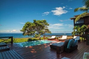 A wooden deck with a pool, lounge chairs, and a view of the ocean. - Cocolobo Resort (Roatan)