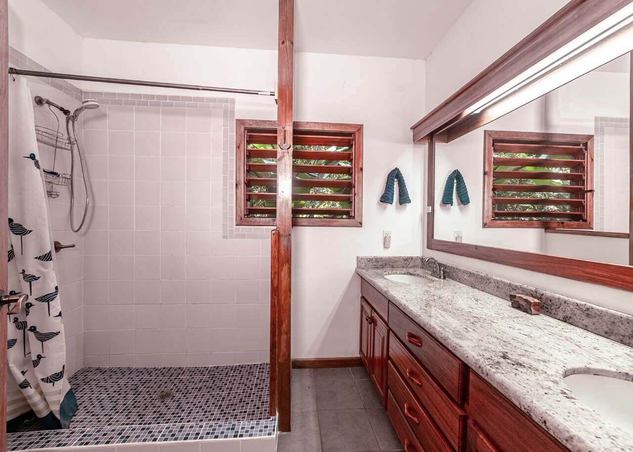 A bathroom with a shower, a sink with a mirror, and a tiled floor.