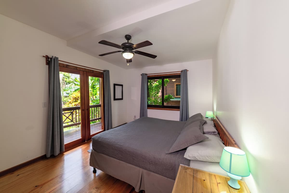 Un dormitorio con cama, ventilador de techo, ventana con cortinas y balcón.