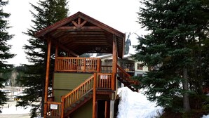 Una cabana de fusta amb una escala i un balcó, envoltada de neu i arbres.