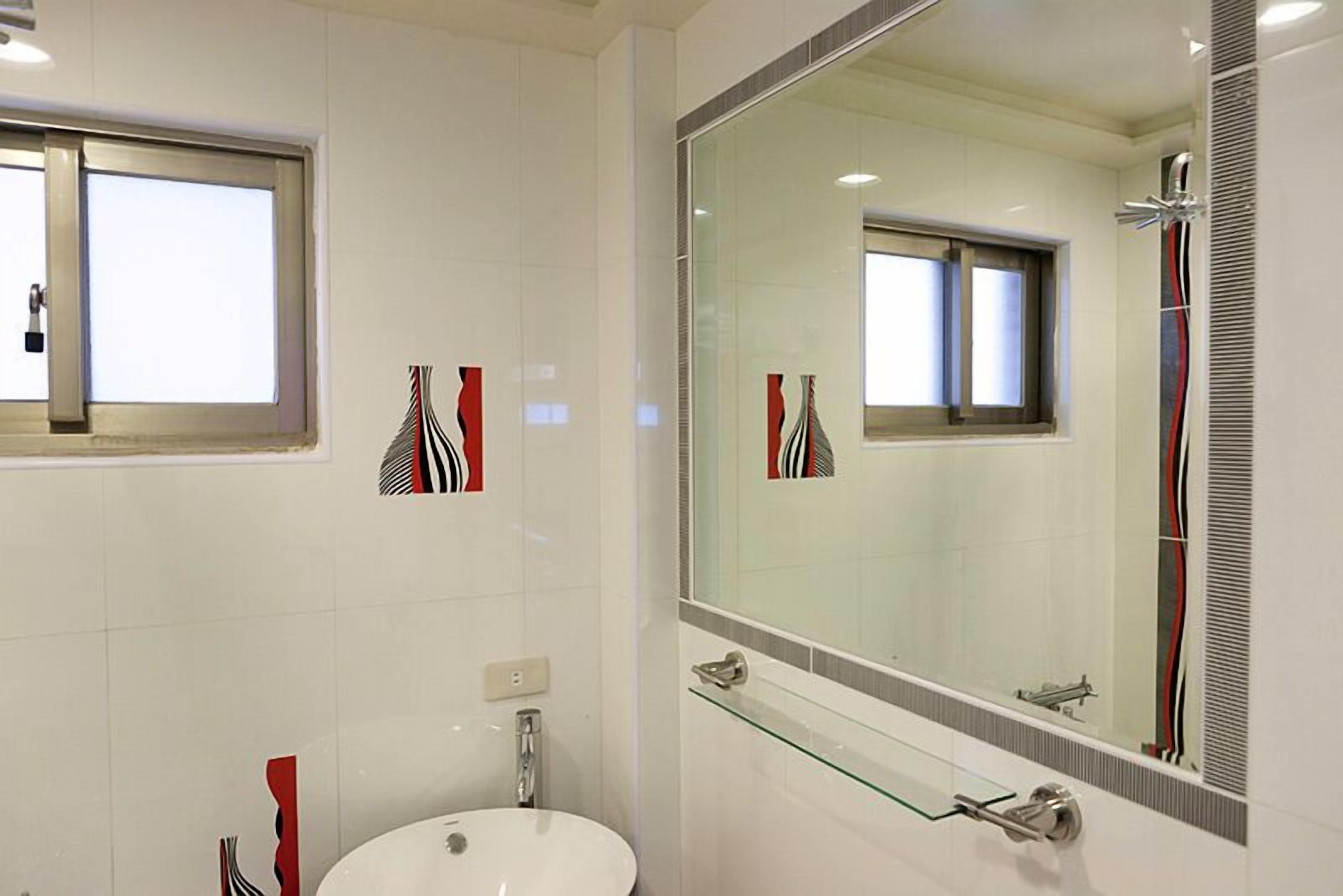 A modern bathroom with a white sink, a large mirror, and a glass shelf.