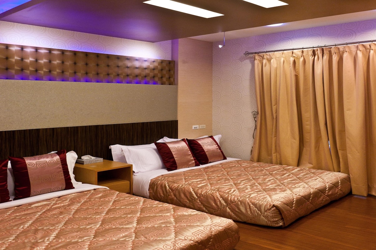 A hotel room with two beds, a wooden headboard, a nightstand, and a curtain.