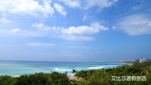 A coastal view with a beach, ocean, and a building in the distance. - Ibiza Kenting Hotel (Hengchun)