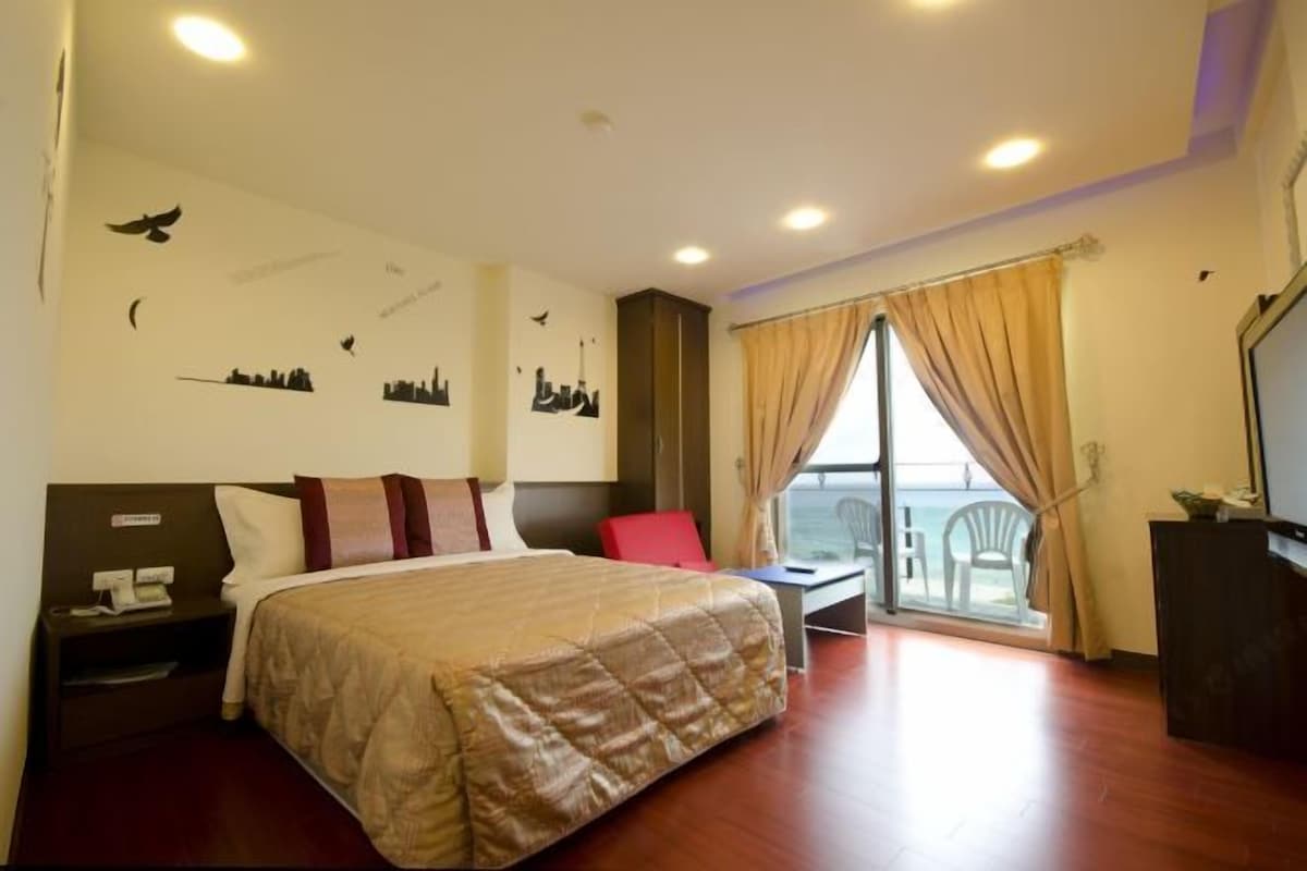Een hotelkamer met een bed, een bureau, een stoel, een televisie en een balkon met uitzicht.