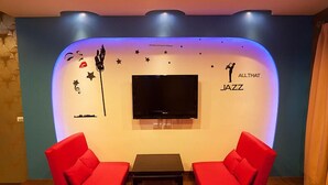 A living room with two red sofas, a flat-screen TV, and a wall with decorative elements including a silhouette of a person playing a saxophone and the words "ALL THAT JAZZ". - Ibiza Kenting Hotel (Hengchun)