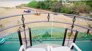 A balcony with a view of a beach, a parking area, and some greenery. - Ibiza Kenting Hotel (Hengchun)