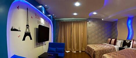 Una habitación de hotel con cama, sofá, televisión y una pared decorada con motivos de la Torre Eiffel y la palabra 'LOVE'.