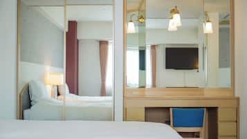 Ein Hotelzimmer mit einem Bett, einem Schreibtisch mit Schubladen, einem Sessel, einem Fernseher und einem großen Spiegel.