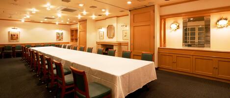 Un salón de conferencias con una larga mesa, sillas verdes y armarios de madera.
