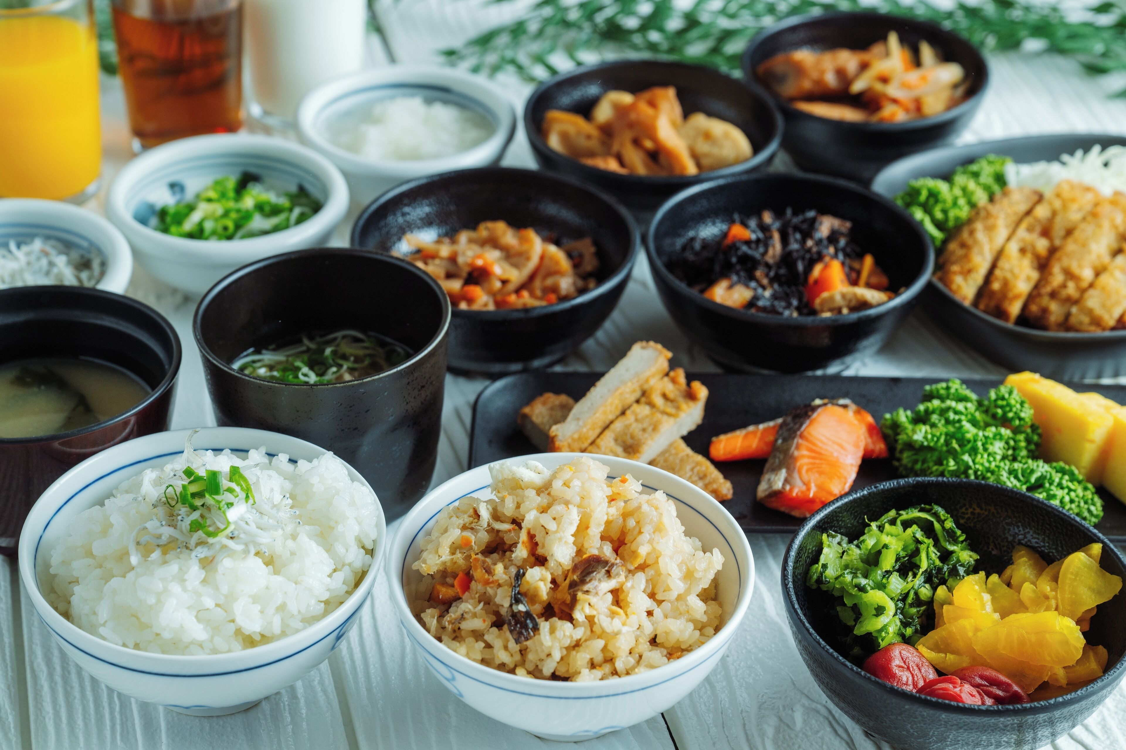 A variety of dishes including rice, vegetables, and meat, served in black bowls on a table.