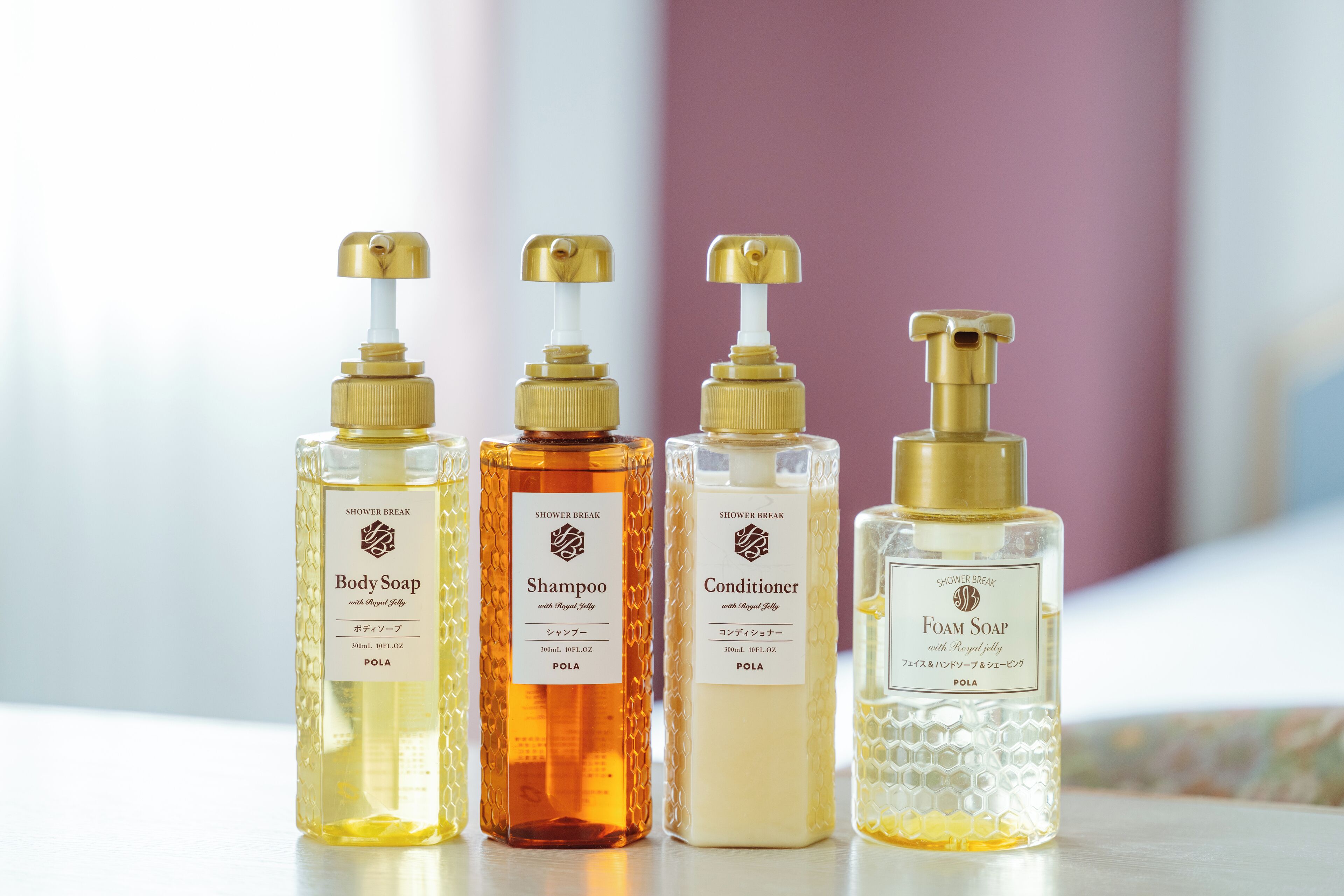 Cuatro botellas de productos de baño con dosificadores, etiquetadas como jabón corporal, champú, acondicionador y jabón espuma.