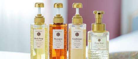 Cuatro botellas de productos de baño con dosificadores, etiquetadas como jabón corporal, champú, acondicionador y jabón espuma.