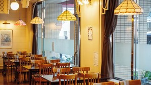 Interior de restaurante con mesas y sillas de madera, lámparas colgantes y vistas por la ventana.
