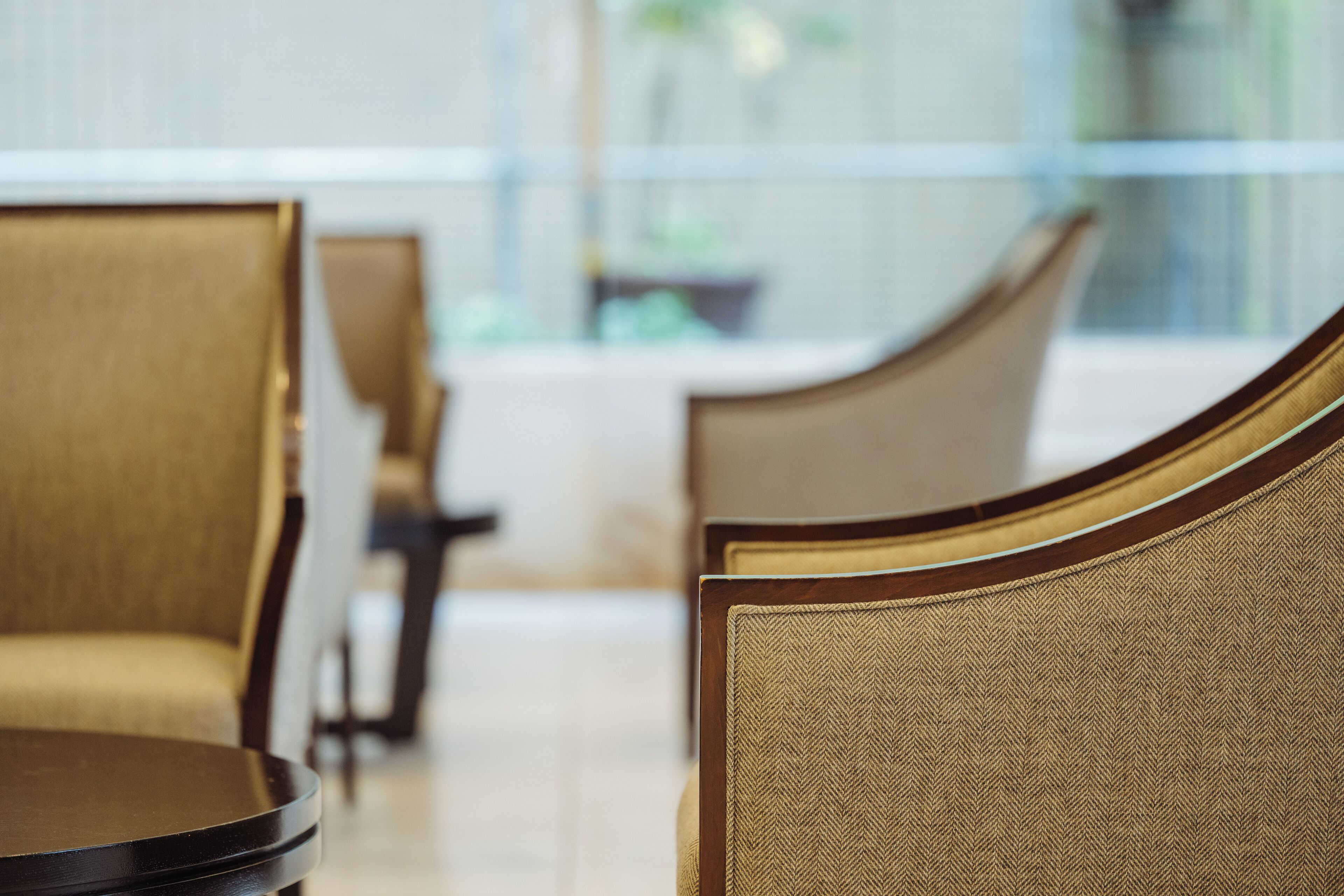 A dining area with round tables and chairs, a glass partition, and a view of the outdoors.