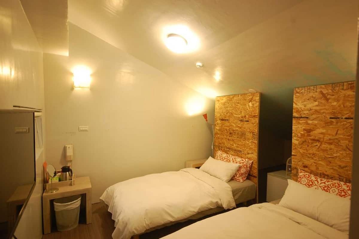 A small, cozy hotel room with two single beds, a small desk with a kettle, and a trash bin.