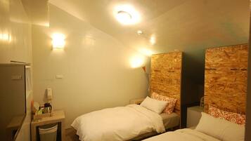 Una habitación de hotel pequeña y acogedora con dos camas individuales, un escritorio pequeño con una tetera y un cubo de basura.