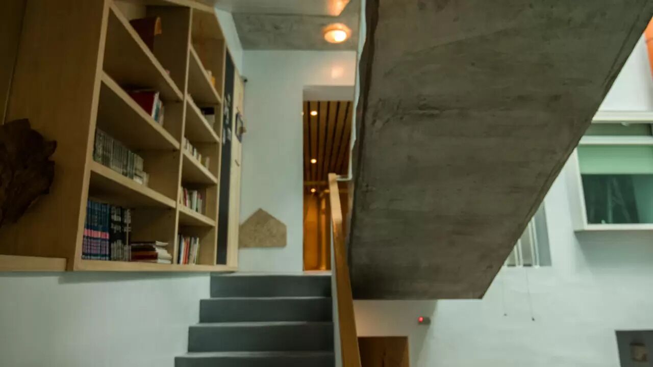 Una escalera con barandilla de hormigón y una estantería de madera a la izquierda.