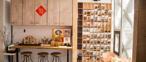 A cozy café with a wooden counter, stools, a bookshelf, and a decorative red sign.