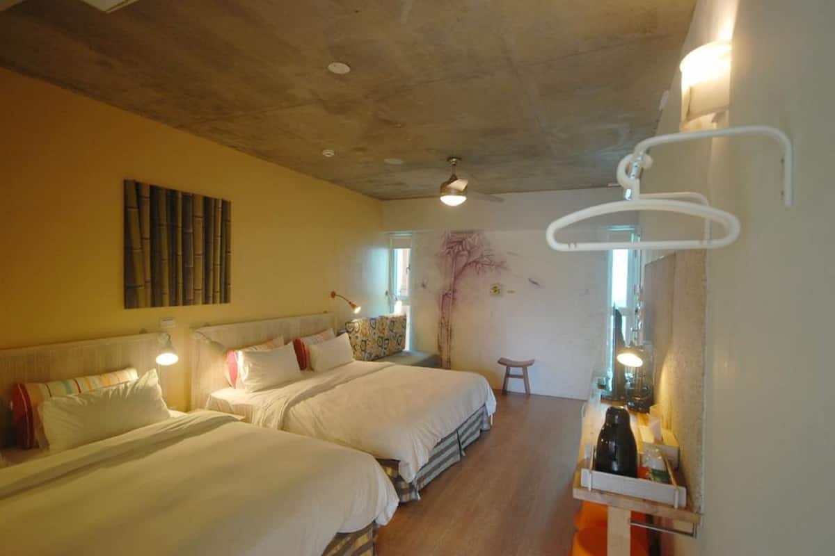 A hotel room with two beds, a wooden floor, a wall-mounted artwork, and a bedside table with a lamp.